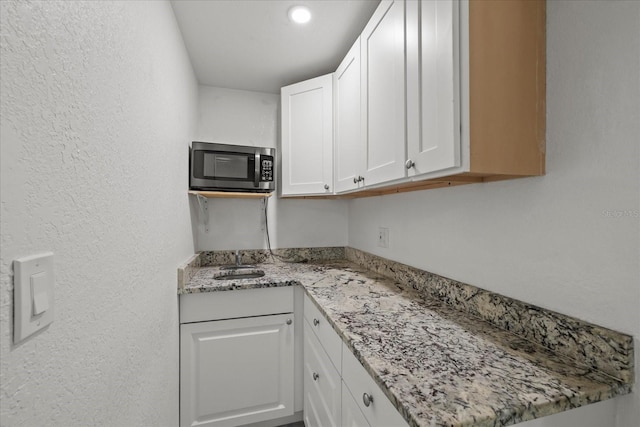 1712 W Atkinson St, Tampa, FL 33604 - kitchen featuring stainless steel microwave, white cabinetry, light stone countertops, and a textured wall