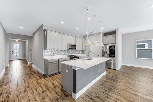 5434 Silver Sun Dr, Apollo Beach, FL 33572 - kitchen with stainless steel appliances, gray cabinetry, backsplash, a center island with sink, and light wood-type flooring