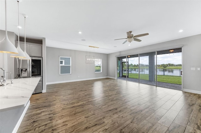 5434 Silver Sun Dr, Apollo Beach, FL 33572 - unfurnished living room with a ceiling fan, dark wood-style flooring, recessed lighting, a chandelier, and a water view