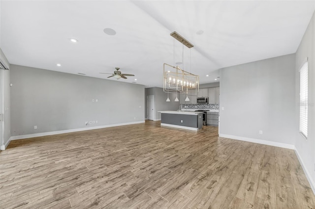 5434 Silver Sun Dr, Apollo Beach, FL 33572 - unfurnished living room featuring light wood-style flooring, ceiling fan, recessed lighting, and a chandelier