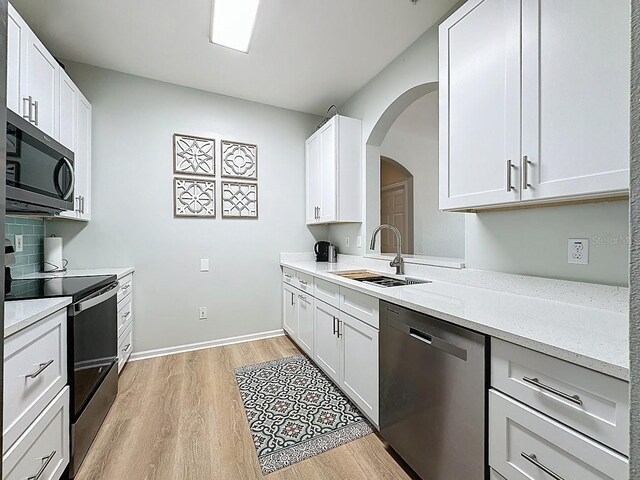 2300 Butterfly Palm Way Unit 204, Kissimmee, FL 34747 - kitchen with appliances with stainless steel finishes, arched walkways, light wood-style floors, white cabinets, and light stone countertops