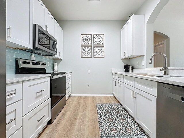 2300 Butterfly Palm Way Unit 204, Kissimmee, FL 34747 - kitchen with stainless steel appliances, light wood-style flooring, decorative backsplash, white cabinets, and arched walkways
