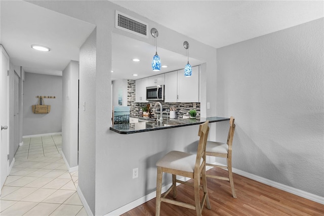 809 Russell Ln Unit 321, Brandon, FL 33510 - kitchen featuring stainless steel microwave, a kitchen breakfast bar, white cabinetry, tasteful backsplash, and dark countertops