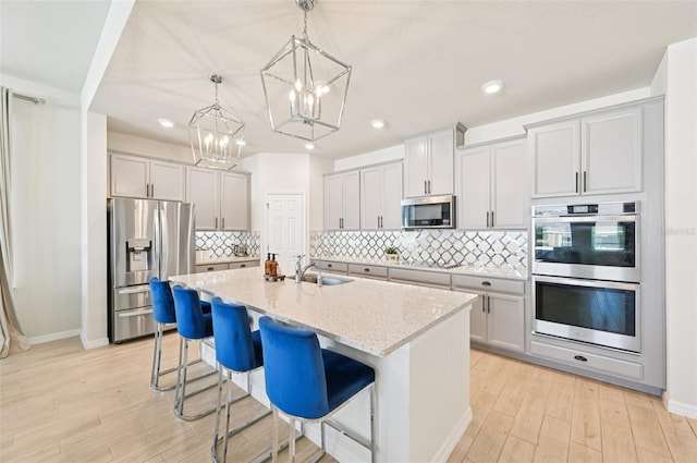 11713 Tetrafin Dr, Riverview, FL 33579 - kitchen featuring stainless steel appliances, a chandelier, light wood-type flooring, light stone counters, and a kitchen island with sink