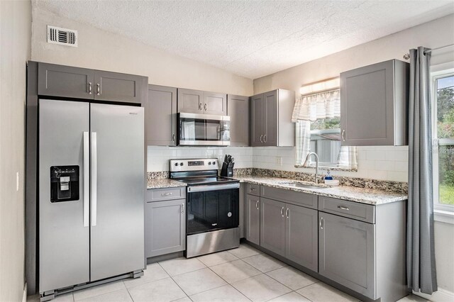 15008 Spokane Rd, Spring Hill, FL 34610 - kitchen with stainless steel appliances, gray cabinets, a textured ceiling, healthy amount of natural light, and tasteful backsplash