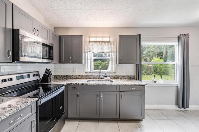 15008 Spokane Rd, Spring Hill, FL 34610 - kitchen featuring appliances with stainless steel finishes, gray cabinetry, backsplash, and a textured ceiling