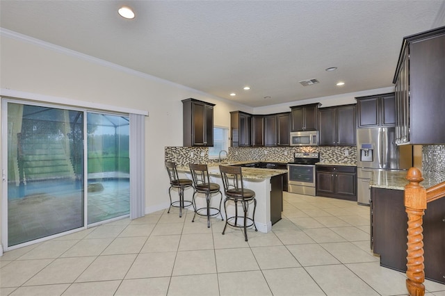 2605 Stardale Way, Lutz, FL 33558 - kitchen featuring appliances with stainless steel finishes, a peninsula, dark brown cabinetry, decorative backsplash, and crown molding
