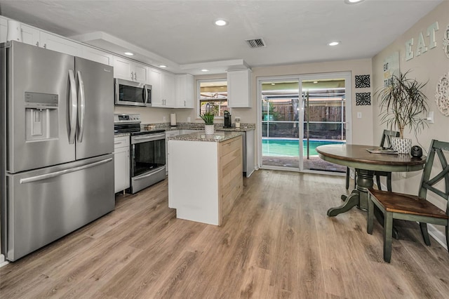 6053 11th Ave, New Port Richey, FL 34653 - kitchen with stainless steel appliances, white cabinets, light stone counters, light wood-style flooring, and recessed lighting