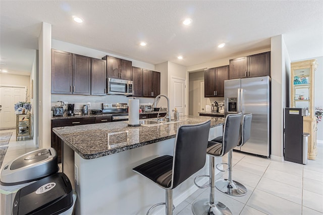 4954 Wild Senna Blvd, Tampa, FL 33619 - kitchen featuring appliances with stainless steel finishes, a breakfast bar, dark brown cabinets, recessed lighting, and dark stone countertops