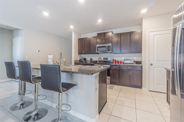4954 Wild Senna Blvd, Tampa, FL 33619 - kitchen with stainless steel appliances, a kitchen bar, a center island with sink, dark brown cabinets, and dark stone countertops