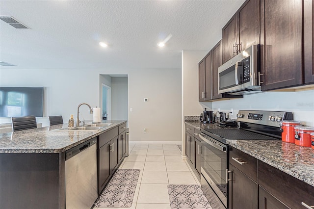 4954 Wild Senna Blvd, Tampa, FL 33619 - kitchen with stainless steel appliances, dark brown cabinetry, a kitchen island with sink, dark stone counters, and a textured ceiling