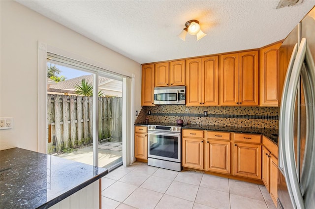 808 Franklin Cir, Palm Harbor, FL 34683 - kitchen featuring appliances with stainless steel finishes, dark stone counters, decorative backsplash, brown cabinetry, and a textured ceiling