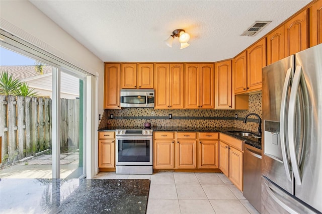 808 Franklin Cir, Palm Harbor, FL 34683 - kitchen featuring stainless steel appliances, dark stone countertops, decorative backsplash, light tile patterned floors, and brown cabinets