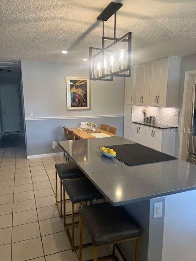4487 Anderson Rd, Orlando, FL 32812 - kitchen with white cabinets, a textured ceiling, dark countertops, light tile patterned floors, and a kitchen island