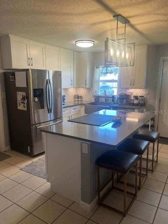 4487 Anderson Rd, Orlando, FL 32812 - kitchen featuring stainless steel fridge, a textured ceiling, white cabinetry, and decorative backsplash