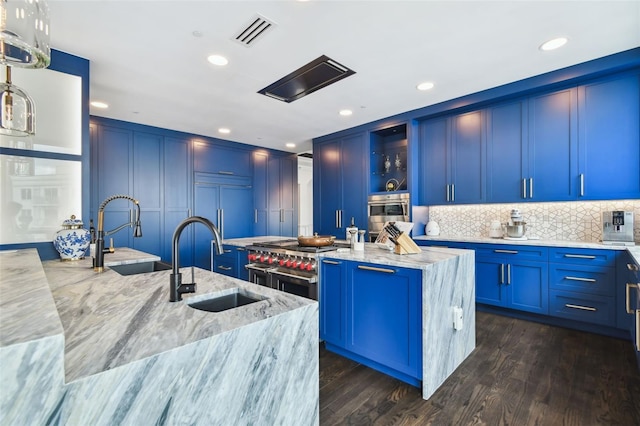 450 Knights Run Ave Unit 2004, Tampa, FL 33602 - kitchen featuring an island with sink, light stone counters, blue cabinets, backsplash, and dark wood-type flooring