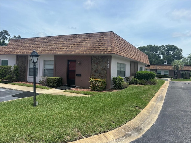 6125 Chesham Dr Unit 1, New Port Richey, FL 34653 - view of front of property featuring mansard roof, a front lawn, roof with shingles, and stone siding
