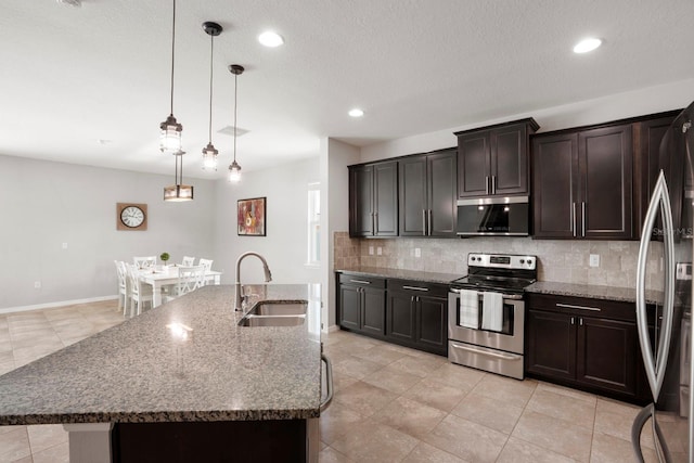 15206 Trinity Fall Way, Bradenton, FL 34212 - kitchen with stainless steel appliances, decorative backsplash, dark stone countertops, hanging light fixtures, and dark brown cabinetry