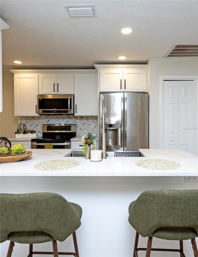 4504 Grainary Ave, Tampa, FL 33624 - kitchen featuring appliances with stainless steel finishes, a breakfast bar area, white cabinetry, backsplash, and recessed lighting