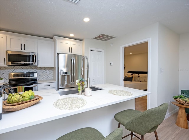 4504 Grainary Ave, Tampa, FL 33624 - kitchen with stainless steel appliances, a breakfast bar area, light wood-style floors, backsplash, and white cabinets