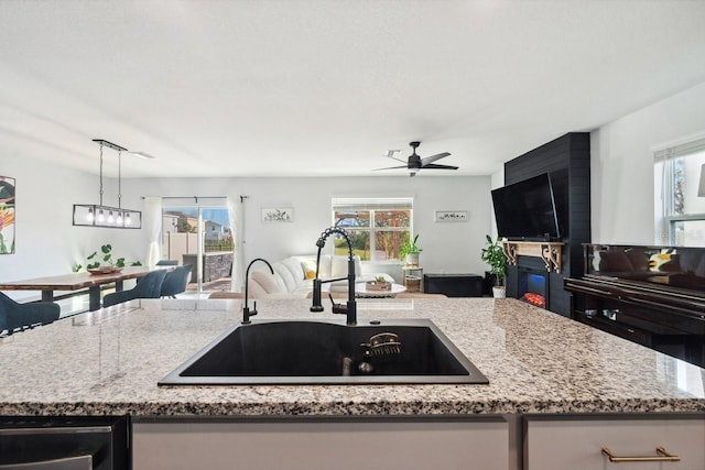 16051 Soft Fern Trce, Odessa, FL 33556 - kitchen featuring open floor plan, light stone countertops, a ceiling fan, a glass covered fireplace, and a center island with sink