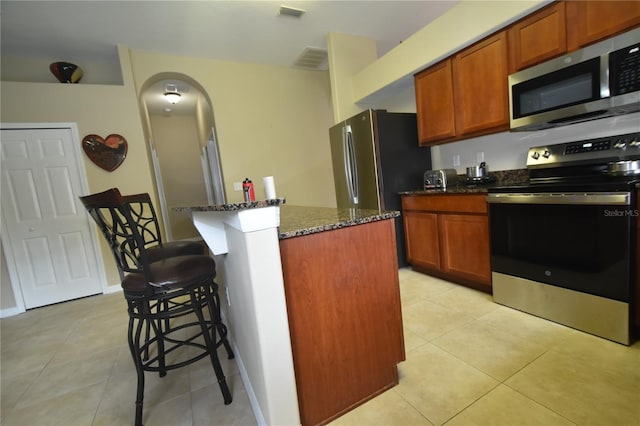 7201 Royal George Ct, Wesley Chapel, FL 33545 - kitchen with stainless steel appliances, dark stone counters, a breakfast bar, arched walkways, and light tile patterned flooring