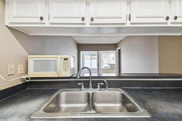 8030 San Bernardino Dr, Port Richey, FL 34668 - kitchen with white microwave, white cabinetry, and dark countertops