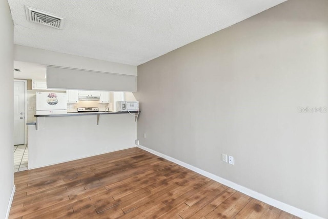 8030 San Bernardino Dr, Port Richey, FL 34668 - kitchen featuring wood finished floors, dark countertops, under cabinet range hood, refrigerator, and a textured ceiling