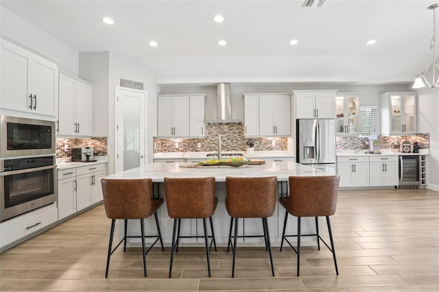 5426 Wayfarer Ave, Apollo Beach, FL 33572 - kitchen featuring stainless steel appliances, wall chimney range hood, beverage cooler, light wood-style floors, and decorative backsplash