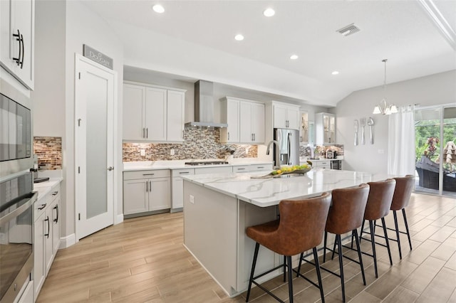 5426 Wayfarer Ave, Apollo Beach, FL 33572 - kitchen featuring wall chimney exhaust hood, stainless steel appliances, light wood-style flooring, tasteful backsplash, and a kitchen breakfast bar