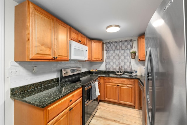 1905 E 99th Ave, Tampa, FL 33612 - kitchen featuring stainless steel appliances, light wood-style flooring, tasteful backsplash, dark stone counters, and brown cabinets