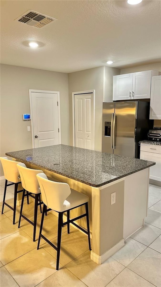 31363 Sun Kettle Loop, Wesley Chapel, FL 33545 - kitchen featuring stainless steel fridge, a kitchen island, dark stone countertops, light tile patterned flooring, and a kitchen breakfast bar