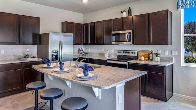 8110 Swan Mist Way, Wesley Chapel, FL 33545 - kitchen featuring stainless steel appliances, a kitchen breakfast bar, dark brown cabinetry, an island with sink, and light tile patterned floors