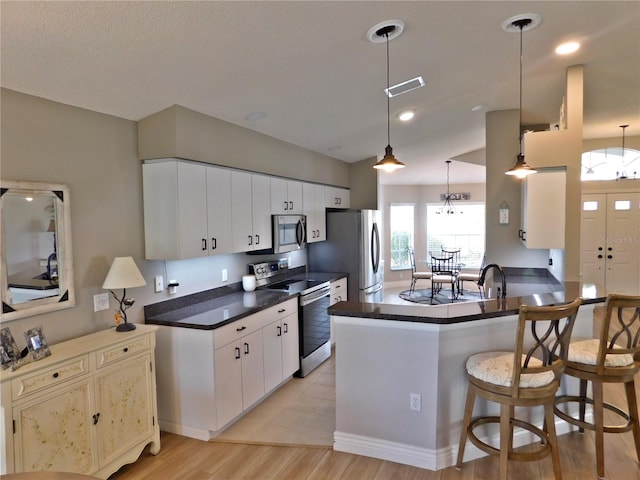 11802 Aintree Ct, Trinity, FL 34655 - kitchen with stainless steel appliances, light wood-style floors, dark countertops, a kitchen bar, and a peninsula
