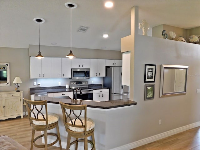 11802 Aintree Ct, Trinity, FL 34655 - kitchen featuring stainless steel appliances, light wood-style floors, dark countertops, white cabinetry, and a breakfast bar