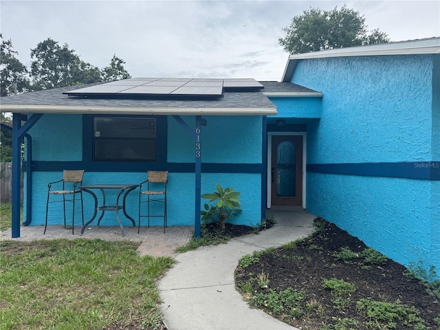 6133 Arthur Ave, New Port Richey, FL 34653 - entrance to property featuring solar panels, stucco siding, roof with shingles, and covered porch