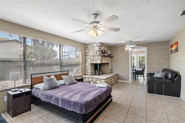 6801 34th Ave W, Bradenton, FL 34209 - bedroom with light tile patterned flooring, a textured ceiling, a stone fireplace, and a ceiling fan