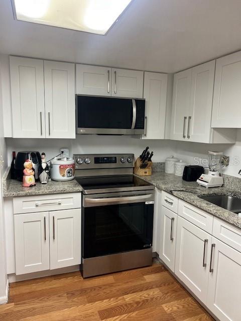 7518 Dolonita Dr Unit 7518, Tampa, FL 33615 - kitchen with appliances with stainless steel finishes, white cabinets, light wood finished floors, and light stone counters