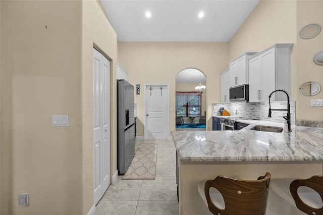 13395 59th Ct N, West Palm Beach, FL 33411 - kitchen featuring stainless steel appliances, light stone countertops, a peninsula, a chandelier, and white cabinets