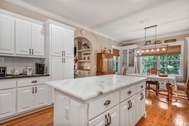 828 E Savoy St, Lecanto, FL 34461 - kitchen with ornamental molding, light wood-type flooring, white cabinets, a kitchen island, and pendant lighting