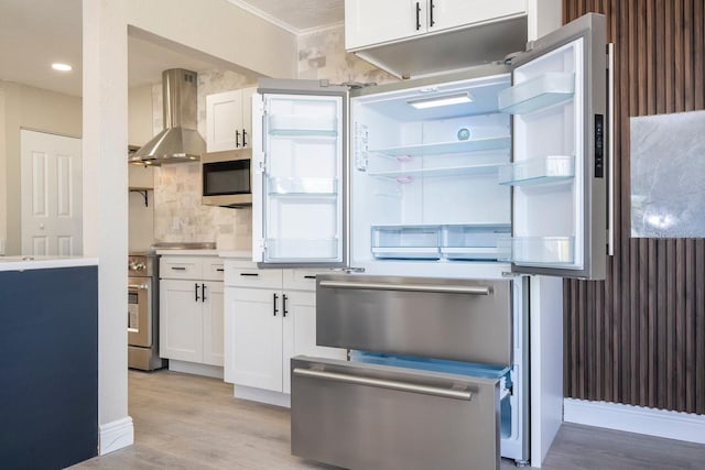 809 59th Ave, Saint Petersburg, FL 33706 - kitchen with wall chimney range hood, stainless steel appliances, light wood finished floors, white cabinetry, and crown molding