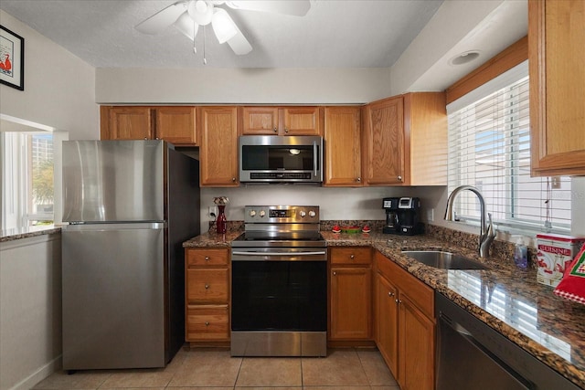 7003 Sunset Way Unit 6, St Pete Beach, FL 33706 - kitchen with stainless steel appliances, ceiling fan, dark stone counters, brown cabinetry, and light tile patterned floors
