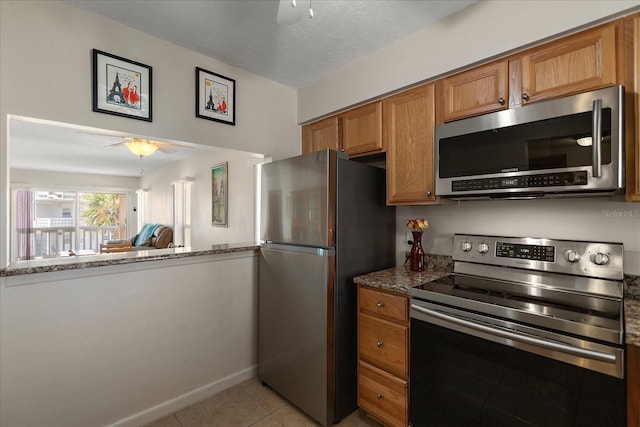 7003 Sunset Way Unit 6, St Pete Beach, FL 33706 - kitchen with stainless steel appliances, ceiling fan, light tile patterned floors, brown cabinetry, and stone counters