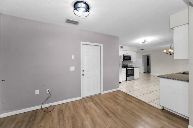 607 Spring Blossom Ct, Brandon, FL 33511 - kitchen featuring appliances with stainless steel finishes, white cabinetry, a chandelier, light wood-style floors, and a textured ceiling