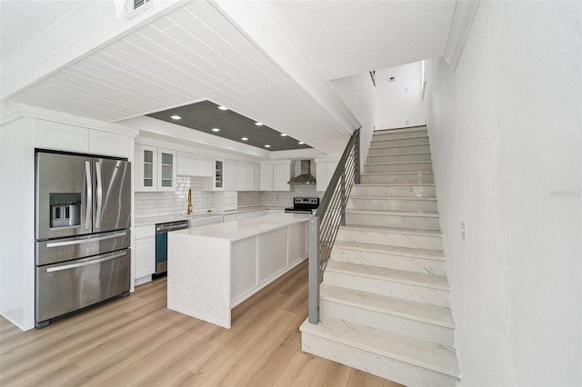 9410 Tara Cay Ct Unit 15, Seminole, FL 33776 - kitchen featuring stainless steel appliances, wall chimney range hood, white cabinetry, decorative backsplash, and light wood-type flooring