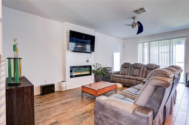 10146 Tuscan Sun Ave, Riverview, FL 33578 - living room with a ceiling fan, a glass covered fireplace, light wood-style floors, and a textured ceiling