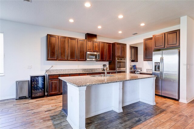 10146 Tuscan Sun Ave, Riverview, FL 33578 - kitchen with appliances with stainless steel finishes, wine cooler, light wood finished floors, light stone counters, and a kitchen island with sink