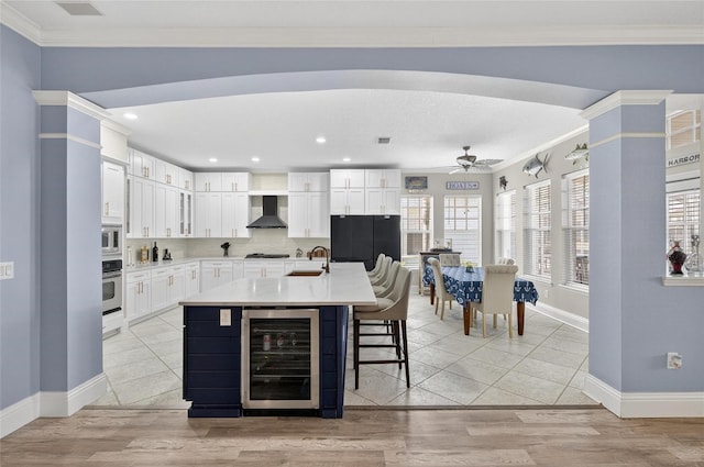 5720 Tortoise Pl, Apollo Beach, FL 33572 - kitchen featuring beverage cooler, wall chimney range hood, appliances with stainless steel finishes, ceiling fan, and a breakfast bar area