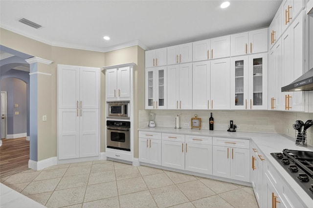 5720 Tortoise Pl, Apollo Beach, FL 33572 - kitchen featuring appliances with stainless steel finishes, arched walkways, tasteful backsplash, wall chimney exhaust hood, and light countertops