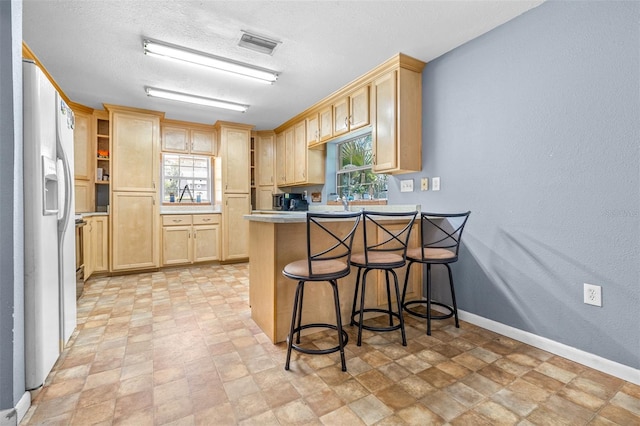 6607 S Merleing Loop, Floral City, FL 34436 - kitchen featuring light brown cabinetry, a peninsula, white refrigerator with ice dispenser, stone finish flooring, and a textured ceiling